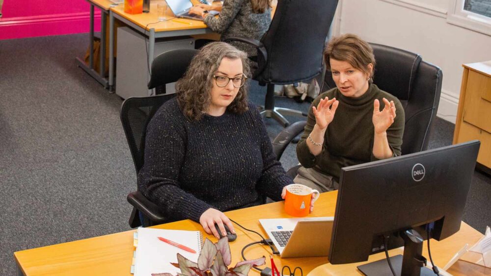 Marketing agency colleagues collaborating at a desk reviewing work on a computer