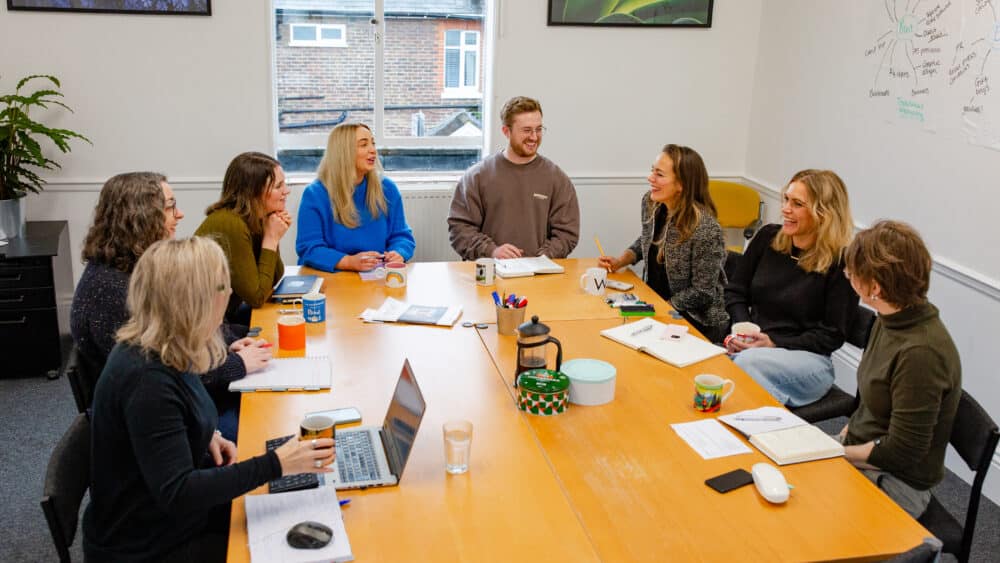 Your Marketing team are sat around a table in a meeting. The team are laughing.