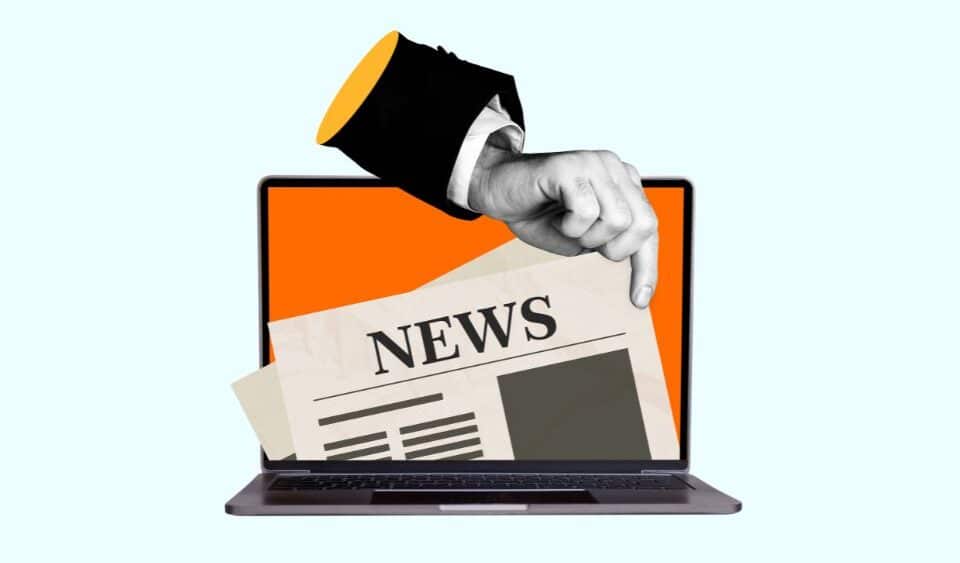 quirky image of a hand wearing a suit jacket and long sleeve shirt picking a newspaper out of a laptop screen