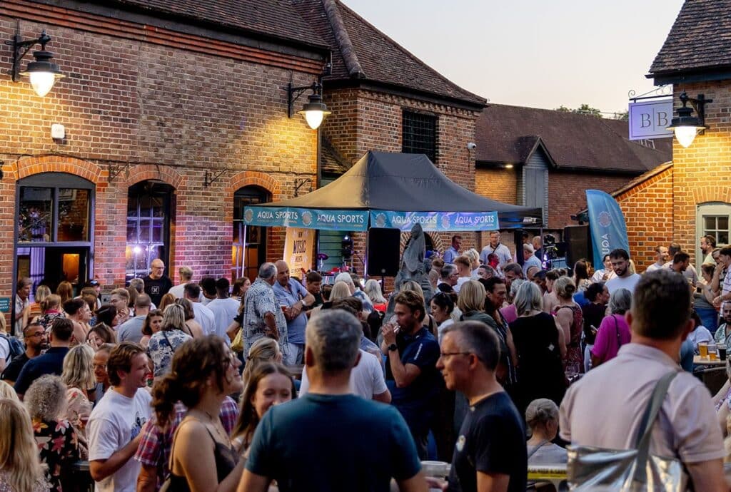 The Cage Yard at Reigate Summer Festival. Lots of people are pictured outside having fun. Aqua Sports sponsored this stage.