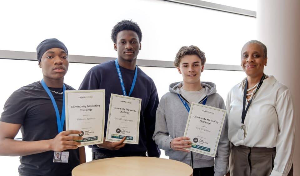 Three smiling boys stand in front of a bright window, holding certificates. Three young men wear lanyards, accompanied by an teacher in a white blouse.