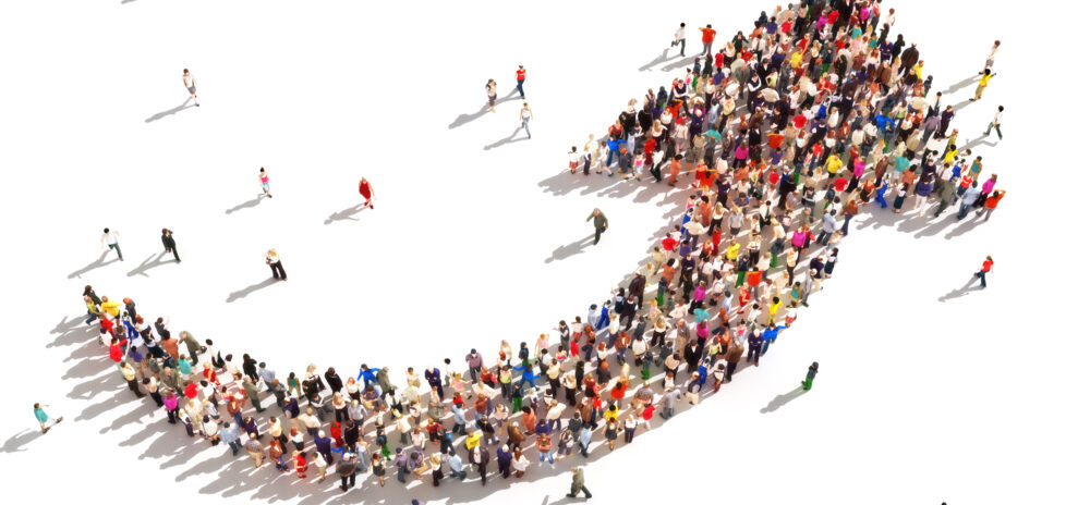 A large crowd of people arranged in the shape of an upward-pointing arrow, viewed from above, suggesting growth, progress, or a movement heading in a positive direction. Marketing budgets.
