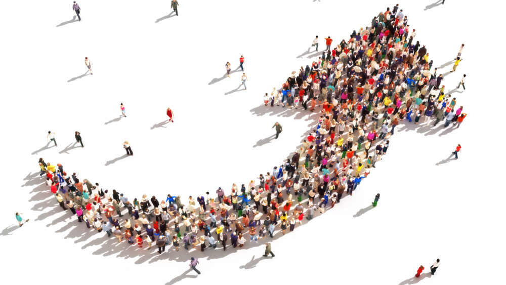 A large crowd of people arranged in the shape of an upward-pointing arrow, viewed from above, suggesting growth, progress, or a movement heading in a positive direction. Marketing budgets.