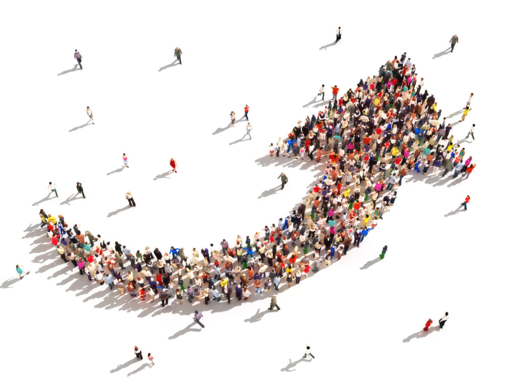 A large crowd of people arranged in the shape of an upward-pointing arrow, viewed from above, suggesting growth, progress, or a movement heading in a positive direction. Marketing budgets.